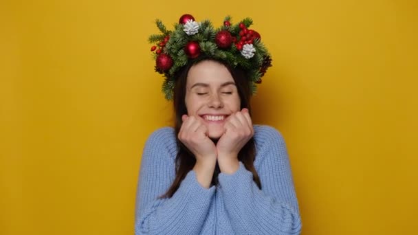 幸せなクリスマスの女性の肖像画は カメラを見て 今後の休日の歓声 黄色の背景に隔離された装飾的な花輪と冬のセーターを身に着けています クリスマスと楽しい時間の概念 — ストック動画
