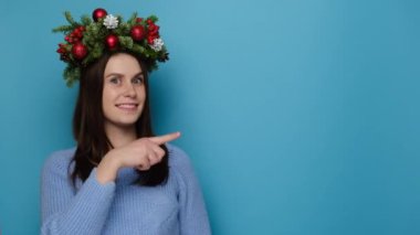 Noel çelengi giymiş güzel bir kız. Boşluğu işaret ediyor. Kış tatilinin tadını çıkarıyor. Bak, senin için ilginç ve harika bir şeyim var. Xmas kutlaması