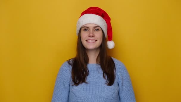 良い見て明るい女性の肖像画は 喜んで 優しい表情で見て 自然の美しさ 笑顔が 黄色の壁に隔離されたクリスマスの赤い帽子と居心地の良い青いセーターを着ている クリスマスお祝い — ストック動画