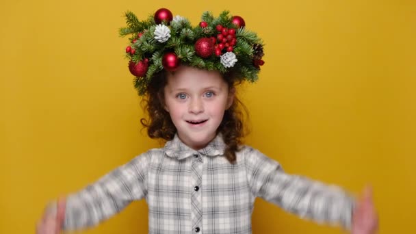 ジェスチャーのように親指を示す幸せな小さな子供の少女の肖像画は 黄色の背景スタジオに隔離された頭の周りのトウヒの休日の花輪を身に着けています お正月のお祝い陽気な休日のコンセプト — ストック動画