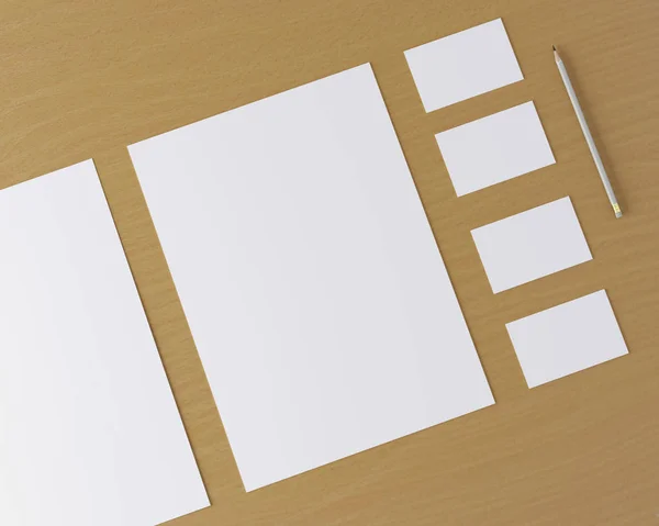 Corporate stationery set mockup. Blank white brand ID elements, paper sheets, card, pencil on a wooden table. Angled top view. 3D rendering.