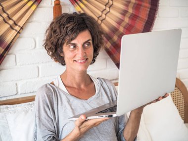 Kadın yatak odasında, ev ofisinde ve karantina konseptinde dizüstü bilgisayar kullanıyor.