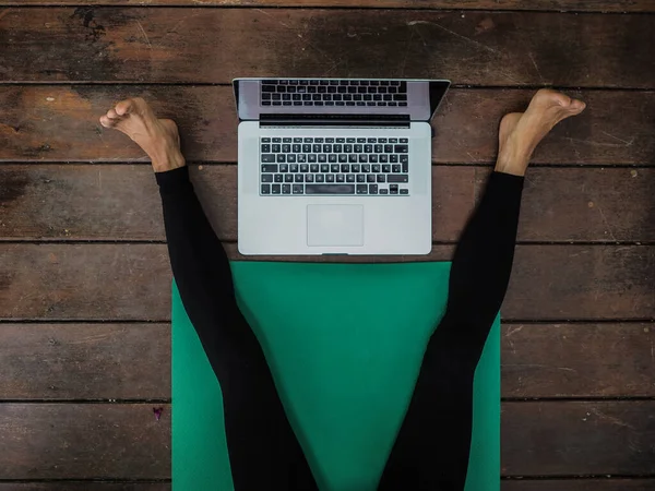 Yoga minderinde dizüstü bilgisayarı yerde yatan kadının bacakları.