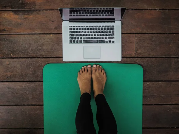 Yoga minderinde dizüstü bilgisayarı yerde yatan kadının bacakları.