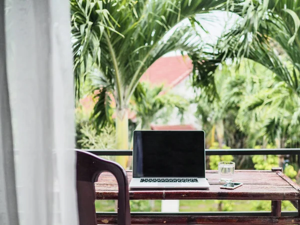 laptop on desk,  green tropical plants on background