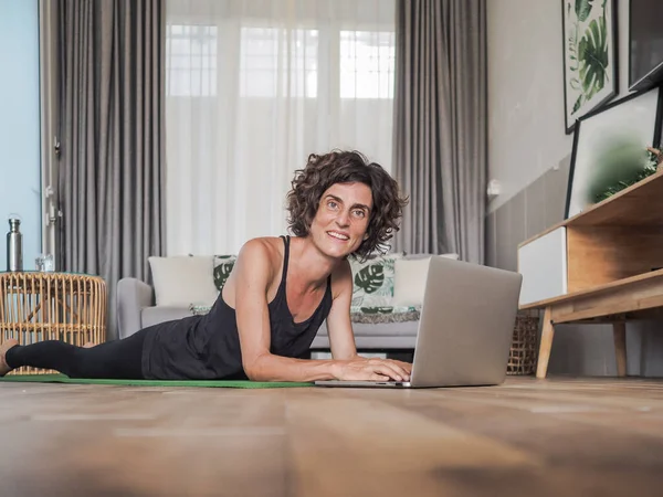 幸せな女性使用ラップトップの家で横たわっヨガマット — ストック写真
