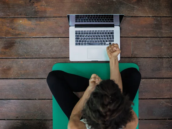 Evde yoga minderinde dizüstü bilgisayar kullanan bir kadın.