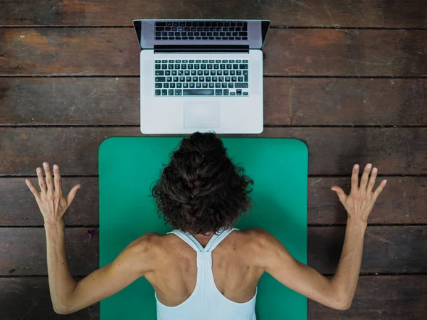 Evde yoga yapan bir kadın dizüstü bilgisayarın önünde oturuyor.