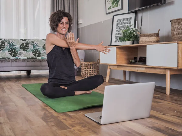 Evde yoga yapan bir kadın dizüstü bilgisayarın önünde oturuyor.