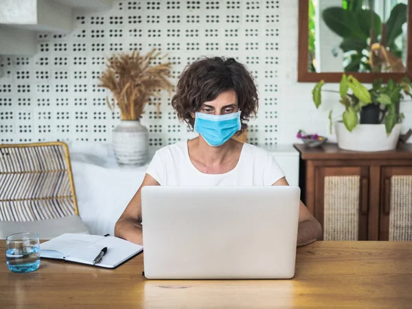 woman wearing mask working with laptop at home, home office and quarantine concept