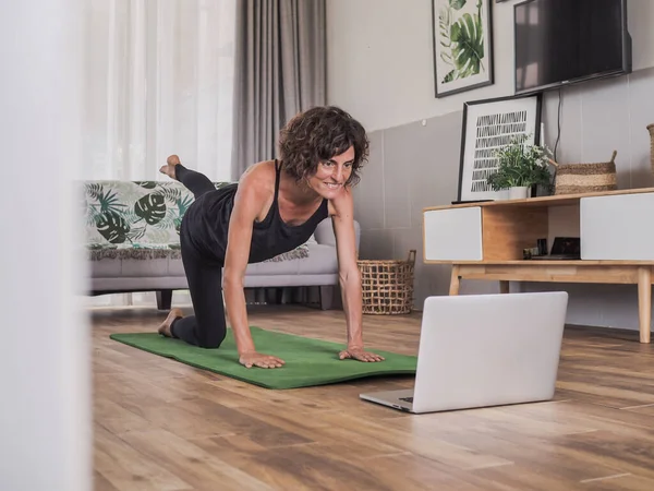 Evde yoga yapan bir kadın dizüstü bilgisayarın önünde oturuyor.