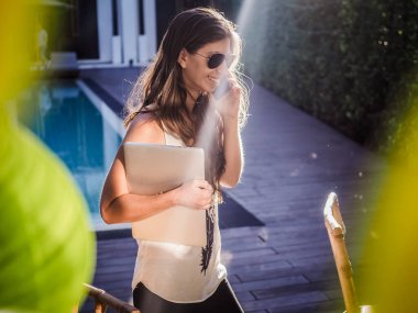 Güzel genç bir kadın dizüstü bilgisayarla sokakta dikilirken akıllı telefondan konuşuyor. 