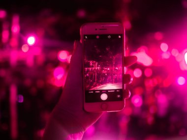 Elinde akıllı telefon tutan ve arka planda bokeh ışıkları olan bir kadın.