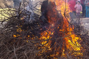 Yanan ateş. Shrovetide içinde büyük şenlik ateşi. Yanan ağaç dalları. İnsanlar ateşe bak. Pagan ayin baharın gelişini adanmış.
