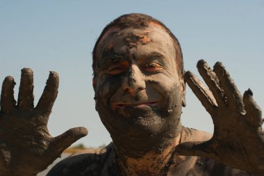 Karadeniz kıyısında Mud Spa tedavileri. Yüzleri yapan kirli bir adamın portresi. Bir adam Bulgaristan'da tatil yapıyor - o olabilir gibi.