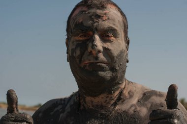 Karadeniz kıyısında Mud Spa tedavileri. Yüzleri yapan kirli bir adamın portresi. Bir adam Bulgaristan'da tatil yapıyor - o olabilir gibi.