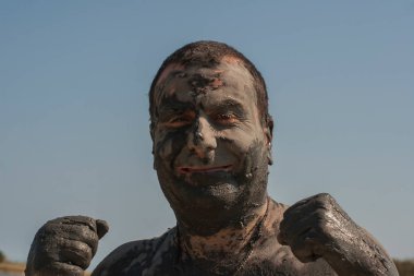 Karadeniz kıyısında Mud Spa tedavileri. Yüzleri yapan kirli bir adamın portresi. Bir adam Bulgaristan'da tatil yapıyor - o olabilir gibi.