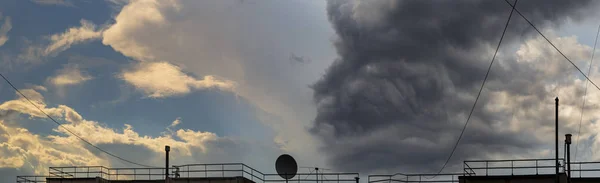 Clouds over the roof of the house. Cumuliform cloudscape on blue sky. Fantastic skies on the planet earth. Shining and gloomy clouds - an allegory of the opposition of good and evil.