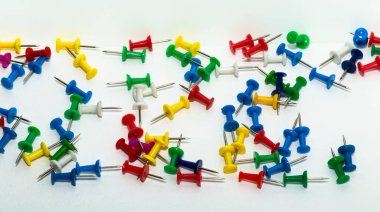 Kağıtları tutturmak için keskin bir iğne. Renkli kırtasiye düğmeleri açık arkaplanda serili. Eğitim için karanfiller. Kağıt iliştiriyorum. Ofis sayfası.