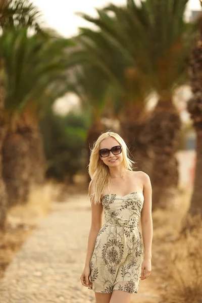 Schöne modische Blondine in kurzem Kleid und Sonnenbrille posiert unter Palmen — Stockfoto