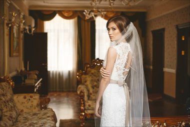 Zarif, duygusal ve güzel esmer modeli kız ile şık düğün saç ve parlak makyaj, moda dantel elbise ile ve lüks iç poz bir örtü ile