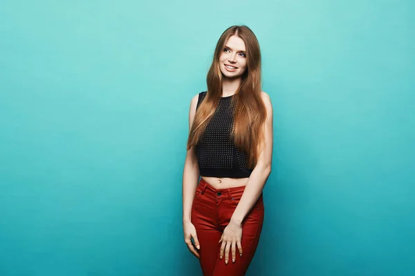 Moderiktiga och vackra blond modell tjej med perfekt kropp i svart snygg t-shirt och trendiga röda byxor poserar på blå bakgrund på sudio, isolerade — Stockfoto