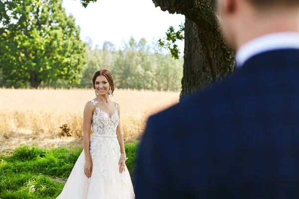 Schöne und modische brünette Modell Mädchen mit hellem Make-up, mit stilvoller Frisur und mit luxuriösen Ohrringen, in modischen Kleid lächelt und posiert unter freiem Himmel — Stockfoto