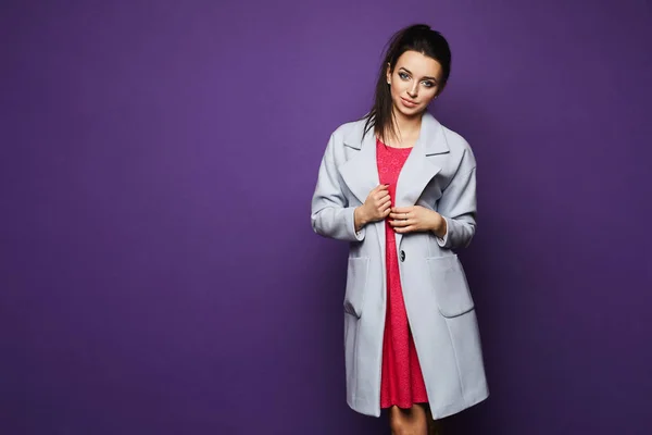 Menina modelo morena sexy e elegante com maquiagem brilhante em vestido rosa elegante curto e em uma capa de chuva na moda posando no estúdio em fundo violeta — Fotografia de Stock