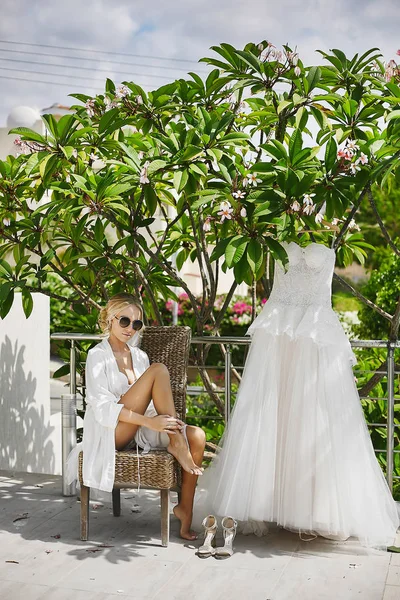 Schöne, vollbusige und modische Blondine, Modelmädchen mit sexy Körper in weißem Peignoir und in Dessous, mit stylischer Sonnenbrille sitzt auf einem Stuhl und genießt die Sonne, die draußen posiert — Stockfoto
