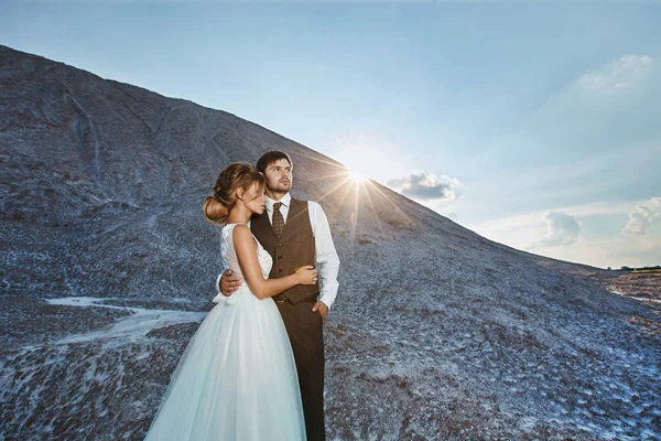 Coppia alla moda e bella, sexy ed elegante ragazza modello bionda con acconciatura elegante, in abito di pizzo bianco e gli uomini belli alla moda in abito alla moda in posa all'aperto al tramonto in montagna — Foto Stock