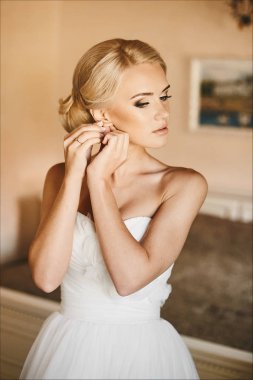Güzel ve şık genç gelin, mavi gözleri ve küpesini ayarlama ve iç, düğün hazırlık sabah poz beyaz elbiseli şık saç modeli ile seksi sarışın model kız