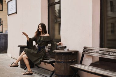 Bir tezgah ve açık havada küçük şehir sokak poz çıplak omuz ile şık elbiseli güzel ve şık esmer modeli kız oturuyor