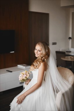 Şehvetli ve mutlu sarışın model kız mavi gözlü ve beyaz elbiseli düğün saç modeli ile iç ve elleri buket ile poz oturur