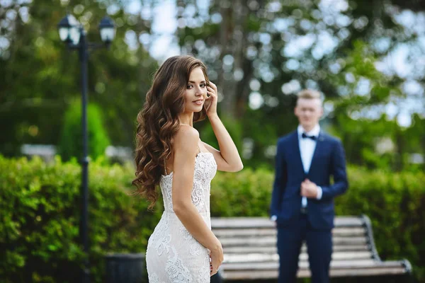 Hermosa y de moda chica modelo morena con cuerpo sexy en vestido de encaje blanco elegante mirando a la cámara y caminando a su novio —  Fotos de Stock