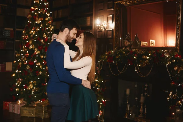 Couple à la mode et beau, fille modèle brune sexy avec un maquillage lumineux dans une jupe et élégant beau barbu hommes câlins et posant près de l'arbre de Noël à l'intérieur décoré pour le Nouvel An — Photo