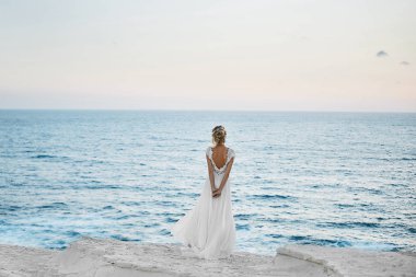 Beyaz elbiseli güzel genç sarışın model kız geri duruyor ve denizde görünüyor