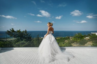 Arka kamera için ayakta ve denize bakarak beyaz elbiseli güzel genç sarışın model kız