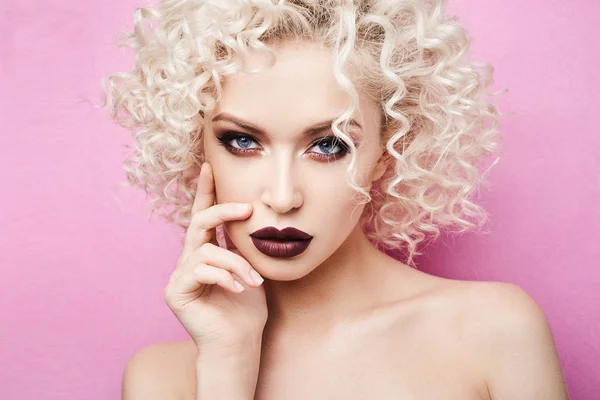 Porträtt av vackra, fasionable och eleganta modell flicka med fantastiska blå ögon, lockigt blont hår och med professionell ljus makeup isolerade på rosa backgroung på studio — Stockfoto