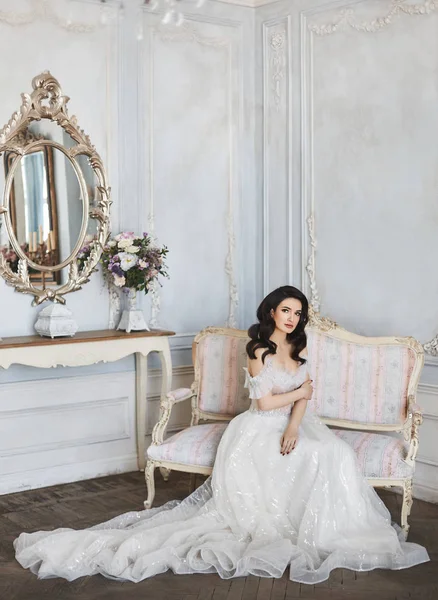 Sensual and beautiful brunette model girl with bright makeup in fashionable lace dress with naked shoulders sits on the antique sofa and posing at luxury vintage interior — Stock Photo, Image