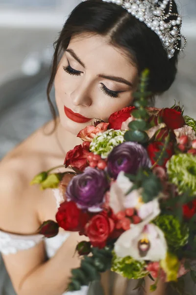 Ung vacker och sexig brunett kvinna, i vit klänning och diadem på hennes huvud, med blommor i händerna — Stockfoto