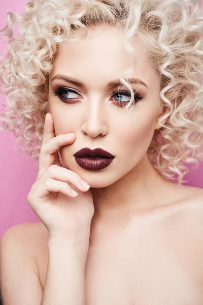 Porträt der schönen und modischen Modell Mädchen mit erstaunlichen blauen Augen, mit lockigen blonden Haaren und mit professionellem hellen Make-up isoliert auf rosa Hintergrund im Studio — Stockfoto