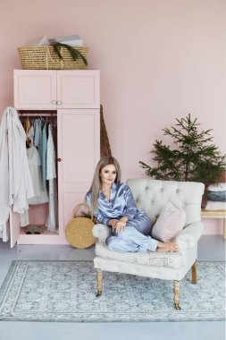Çekici ve güzel sarışın model kız moda Saten Pijama vintage koltuk ve poz hafif pembe iç oturur.