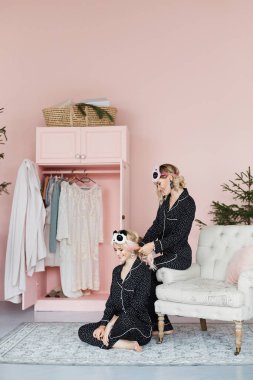İki güzel, mutlu ve gülümseyen sarışın kız moda pijama ve şık pandalar sit vintage kanepede ve yerdeki şeklinde maskeleri uyku ve iç poz model