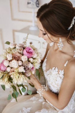 Güzel ve mutlu şık düğün saç moda gelinlik modeli ile esmer modeli kız koltuğa oturur ve vintage iç, onun elinde bir buket ile poz