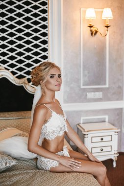 Vintage iç de güzel uzun bacaklı sarışın model kız mükemmel sportif vücut ve şık düğün saç modeli şık beyaz dantel iç çamaşırı ile oturur