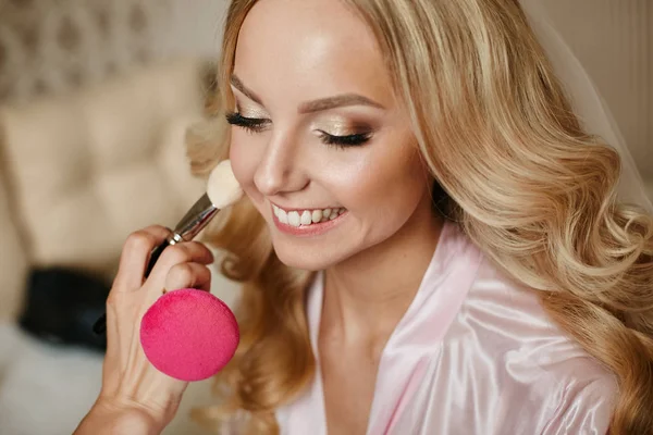 Visagiste aplica maquillaje para una hermosa chica rubia con peinado de boda y sonrisa brillante — Foto de Stock