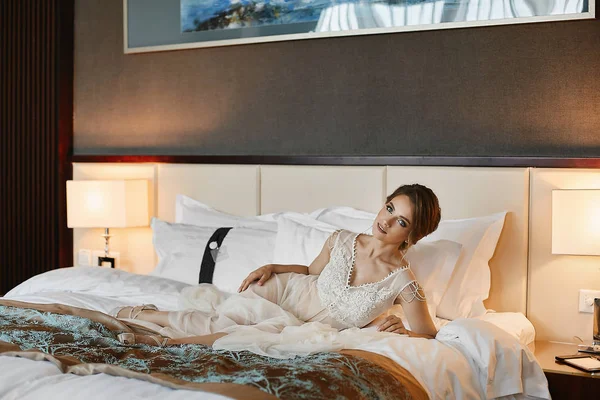 Hermosa chica modelo morena con maquillaje brillante y cuerpo sexy en peignoir de moda larga y lencería elegante en la cama — Foto de Stock