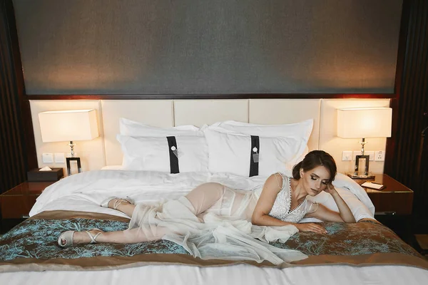 Güzel esmer model kız parlak makyaj ve uzun şık sabahlığı ve yatakta şık iç çamaşırı seksi vücut ile — Stok fotoğraf