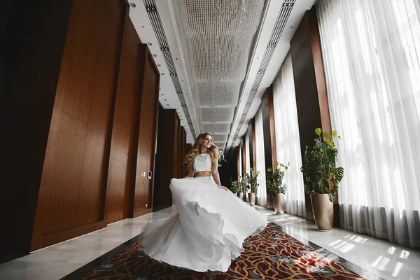 Bella e felice ragazza modello bionda in una gonna elegante e camicetta alla moda corre lungo il corridoio all'interno moderno — Foto Stock