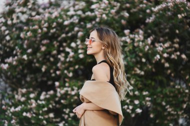 Güzel gülümseme kolsuz ceket ve şık güneş gözlüğü ile şık ve seksi sarışın model kız